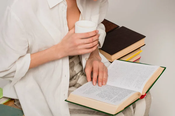 Vista recortada del libro de lectura de la mujer y la celebración de taza de café aislado en gris - foto de stock