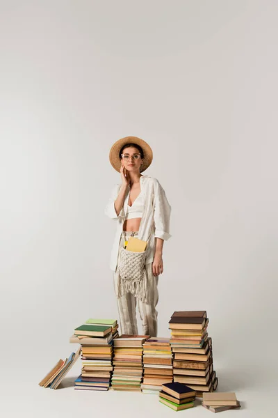 Heureux jeune femme en chapeau de soleil debout près de pile de livres isolés sur blanc — Photo de stock