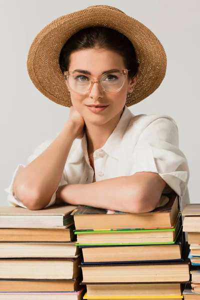 Zufriedene Frau mit Sonnenhut und Brille, angelehnt an einen Stapel Bücher, isoliert auf weißem Grund — Stockfoto