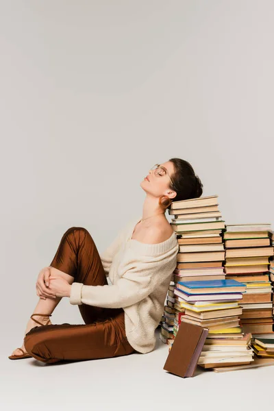 Pleine longueur de jeune femme en lunettes et pull appuyé sur la pile de livres sur blanc — Photo de stock