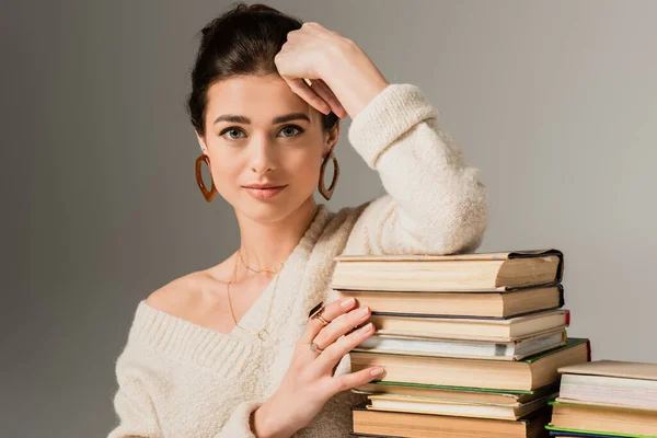 Jovem mulher em brincos apoiando-se na pilha de livros em cinza — Fotografia de Stock