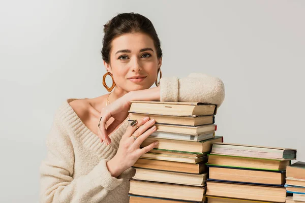 Mujer joven complacida en pendientes apoyados en la pila de libros aislados en blanco - foto de stock