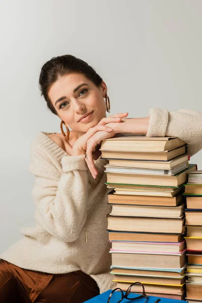 Giovane donna in orecchini appoggiata su pila di libri isolati su bianco — Foto stock