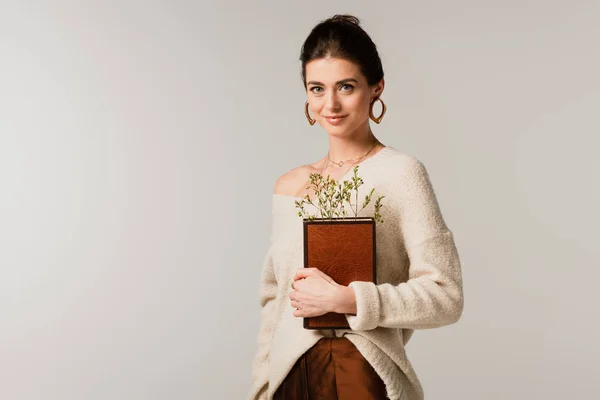 Jovem mulher feliz segurando livro com flores silvestres isolado em cinza — Fotografia de Stock