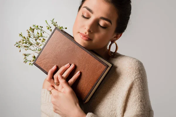 Молодая женщина с закрытыми глазами держит книгу с полевыми цветами, изолированными на сером — стоковое фото