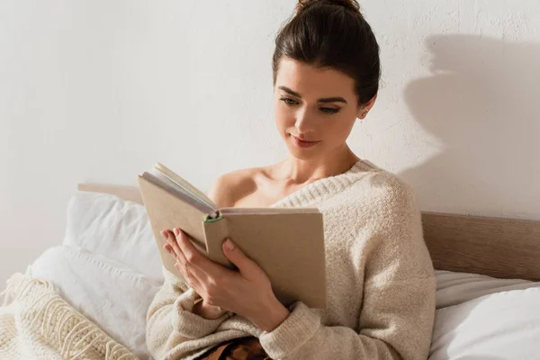 Jolie jeune femme lecture livre tout en se reposant sur le lit à la maison — Photo de stock