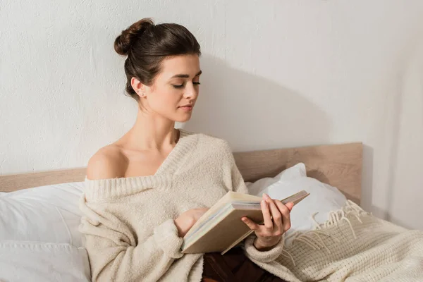 Брюнетка молодая женщина, читающая книгу во время отдыха на кровати дома — стоковое фото
