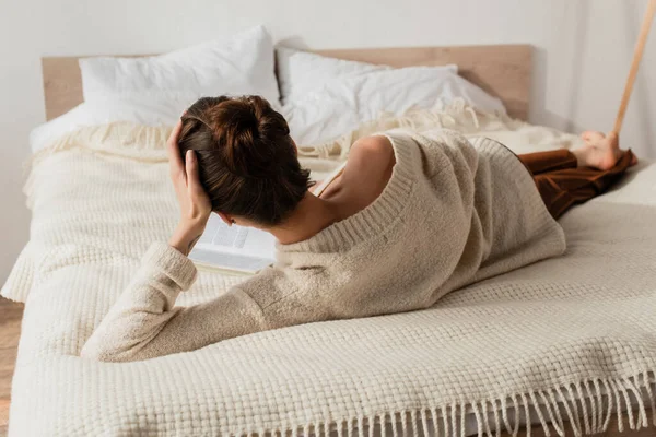 Vue arrière du livre de lecture de jeune femme tout en se reposant sur le lit à la maison — Photo de stock