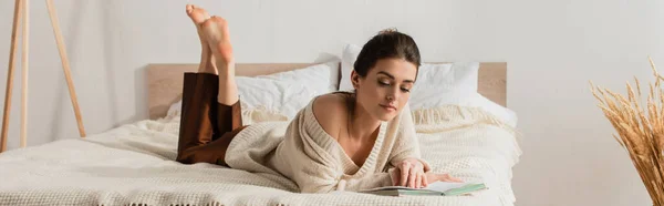 Barefoot young woman reading book while resting on bed, banner — Stock Photo