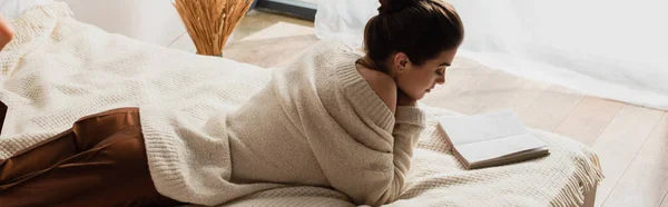 Mujer joven leyendo libro mientras descansa en la cama, pancarta - foto de stock