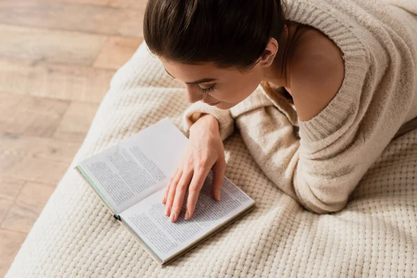 Высокий угол зрения молодой женщины, читающей книгу во время отдыха на кровати дома — стоковое фото