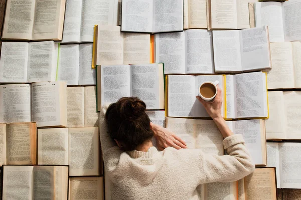 Ansicht von oben: Müde Frau schläft neben offenen Büchern mit einer Tasse Kaffee — Stockfoto