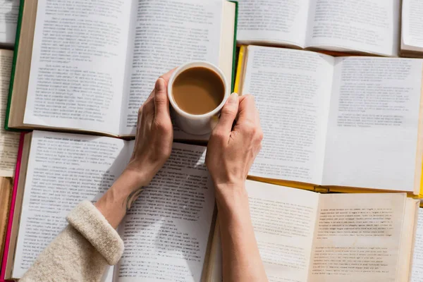 Partial view of woman holding cup of coffee near open books — Stock Photo