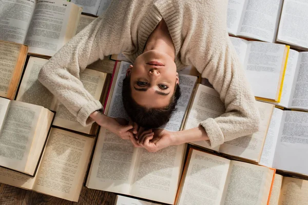 Vista dall'alto di bella donna sdraiata su mucchio di libri aperti — Foto stock