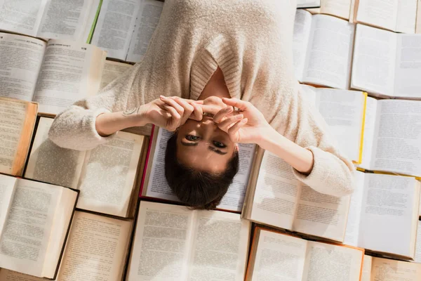 Top view of tattooed woman lying on pile of open books — Stock Photo