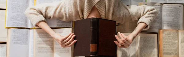 Вид зверху татуйованої жінки затемнює обличчя, лежачи на купі відкритих книг, банер — стокове фото