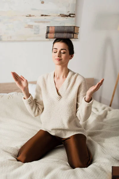 Задоволена жінка з книгами на голові сидить на ліжку — стокове фото