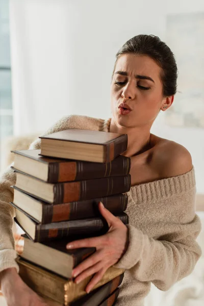 Молода жінка дивиться на купу книг вдома — стокове фото