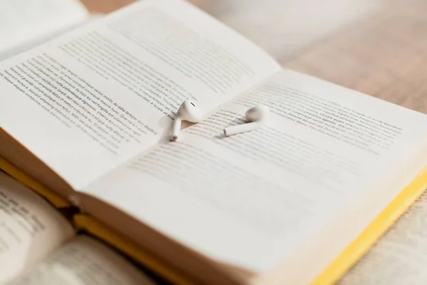 White and wireless earphones on blurred book — Stock Photo