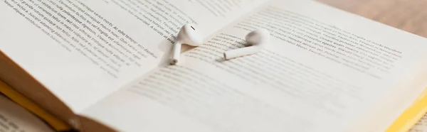 White wireless earphones on blurred book, banner — Stock Photo