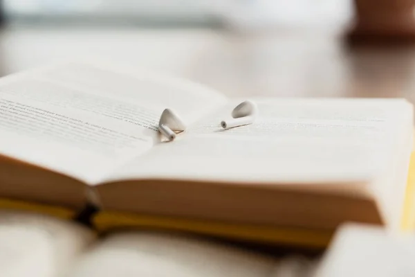 White wireless earphones on blurred book — Stock Photo