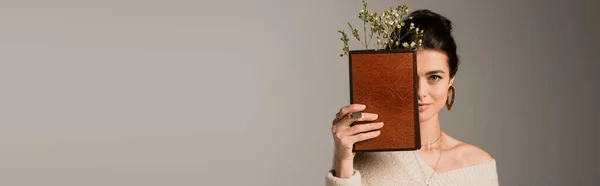 Joven mujer sosteniendo libro en tapa dura con flor aislada en gris, bandera - foto de stock