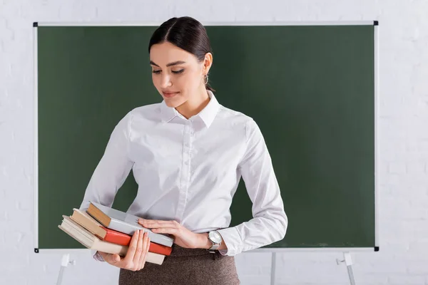 Young teacher looking at books in classroom — Stock Photo
