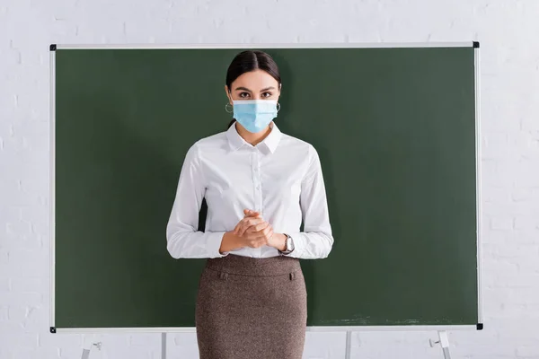 Teacher in medical mask looking at camera in classroom — Stock Photo
