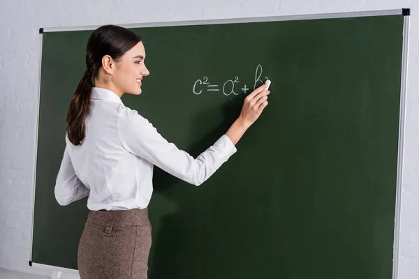 Insegnante sorridente che scrive equazione matematica sulla lavagna — Foto stock