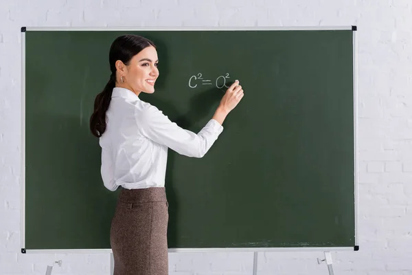 Allegro insegnante con gesso scrittura equazione matematica sulla lavagna — Foto stock