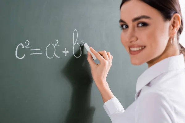 Blurred teacher smiling at camera while writing mathematic formula — Stock Photo