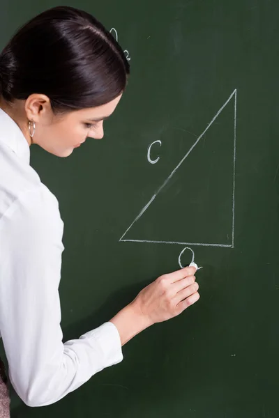 Teacher writing triangle on chalkboard in classroom — Stock Photo