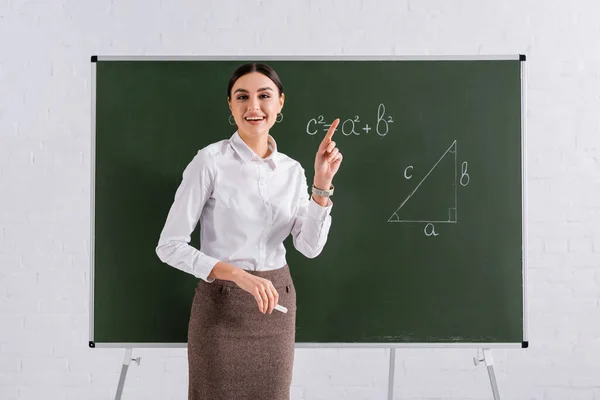 Lächelnder Lehrer zeigt mit Finger auf Kreidetafel mit mathematischer Formel — Stockfoto