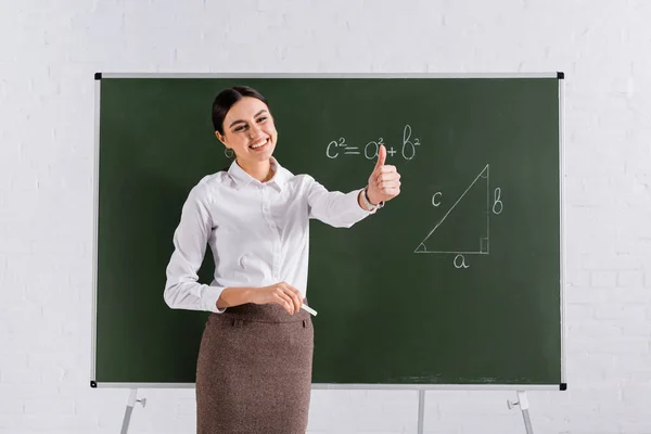 Smiling teacher with chalk showing like near chalkboard with equation — Stock Photo