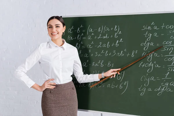 Profesor feliz señalando ecuaciones matemáticas en el aula - foto de stock