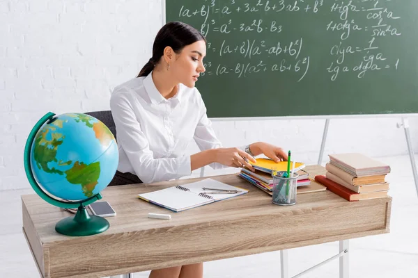 Profesor sosteniendo portátil cerca de libros, teléfonos inteligentes y globo - foto de stock