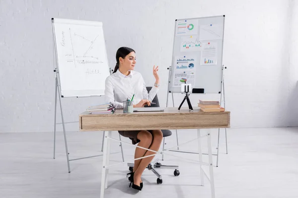 Geschäftsfrau mit Videoanruf auf Smartphone in der Nähe von Flipcharts mit Grafiken — Stockfoto