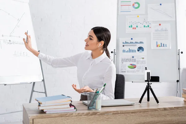 Smiling businesswoman in earphone having video call near flipcharts in office — Stock Photo