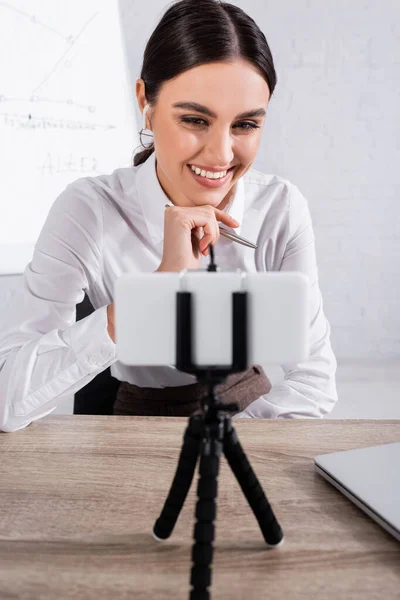 Empresária alegre no fone de ouvido ter vídeo chat no smartphone borrado no escritório — Fotografia de Stock