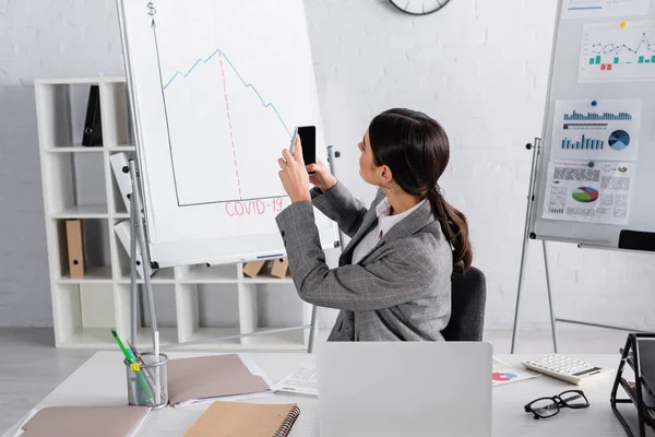 Geschäftsfrau fotografiert Flipchart in der Nähe von Laptop im Büro — Stockfoto