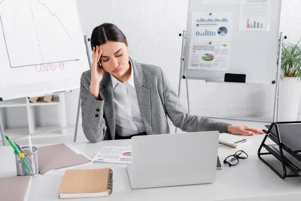 Mujer de negocios cansada sentada cerca de la calculadora, papeles y computadora portátil - foto de stock