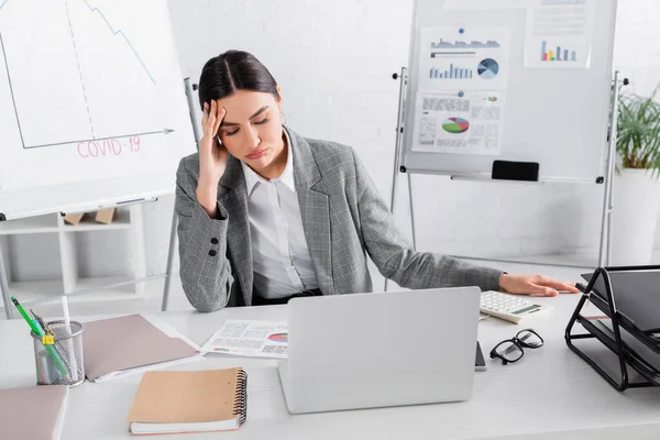 Donna d'affari stanca seduta vicino alla calcolatrice, carte e laptop — Foto stock