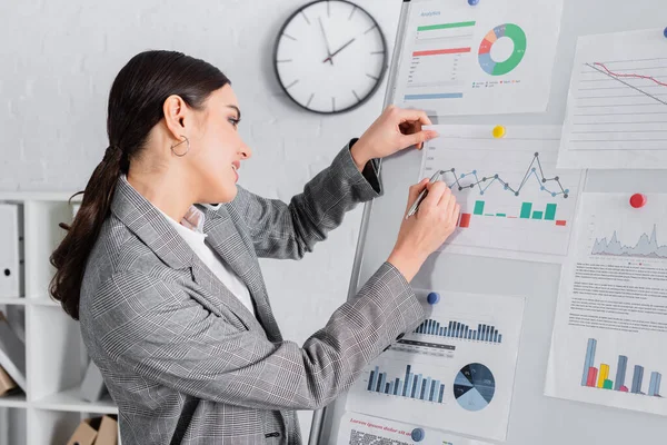 Smiling businesswoman talking on smartphone and holding pen near charts on flipchart — Stock Photo