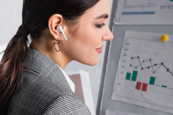 Side view of businesswoman in earphone standing near blurred flipchart — Stock Photo