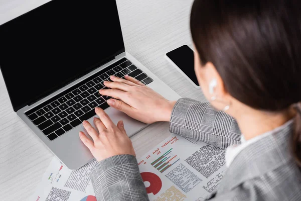Blurred businesswoman using laptop with blank screen near papers with charts — Stock Photo