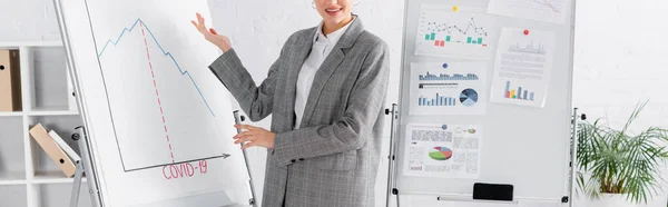 Vista cortada de mulher de negócios sorridente apontando para flipchart com letras covid-2019, banner — Fotografia de Stock
