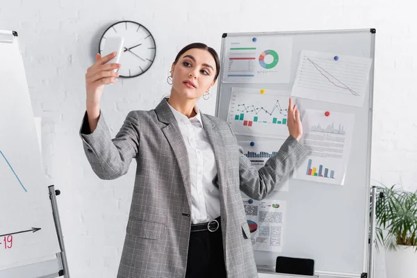 Businesswoman having video call on smartphone near charts on flipchart — Stock Photo