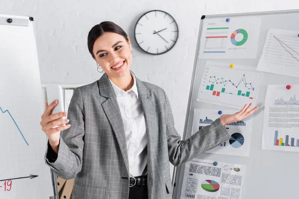 Smiling businesswoman in earphones pointing at flipchart during online meeting — Stock Photo