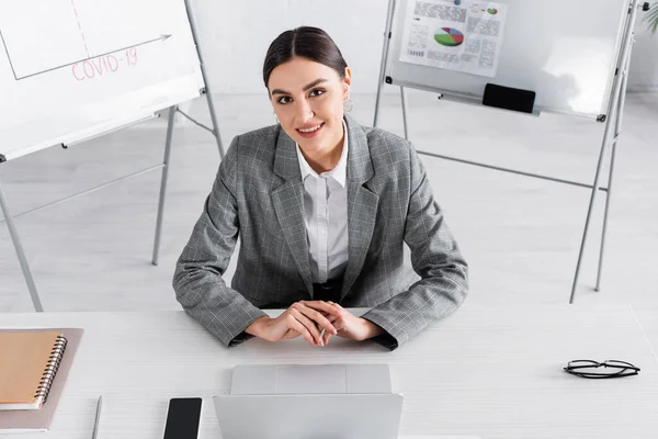 High angle view of businesswoman smiling at camera near devices on working table — Stock Photo