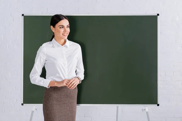 Morena professor em desgaste formal sorrindo perto de quadro-negro — Fotografia de Stock